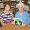 <p>Becky Mondrage (left) and Jean Raines have worked tirelessly to organize the fourth annual Sandlick Homecoming. Raines displays a community cookbook created especially for the celebration, along with a calendar, which includes the history of Sandlick and stories about some of its people.</p>